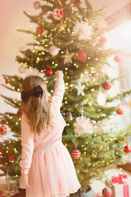 Menina de vestido rosa pendurado ornamentos na árvore de Natal — Fotografia de Stock