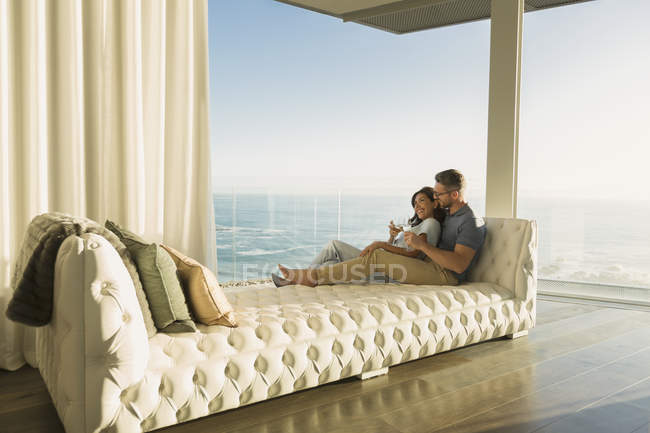 Casal afetuoso beber vinho no salão de chaise tufado com vista para o mar — Fotografia de Stock