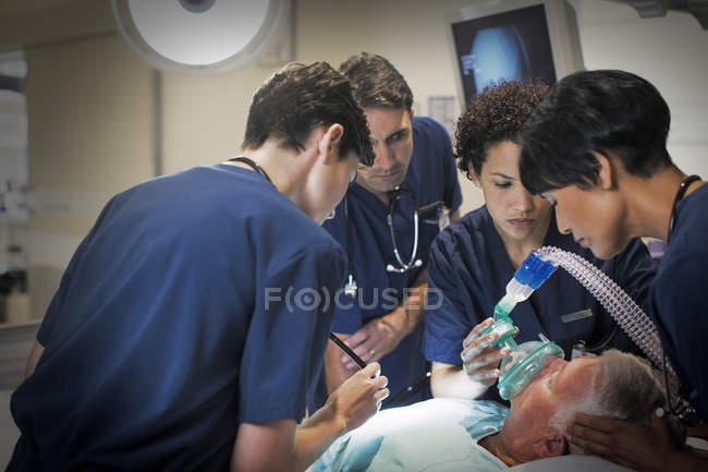 Médica usando máscara enquanto anestesiava paciente idoso na enfermaria do hospital — Fotografia de Stock