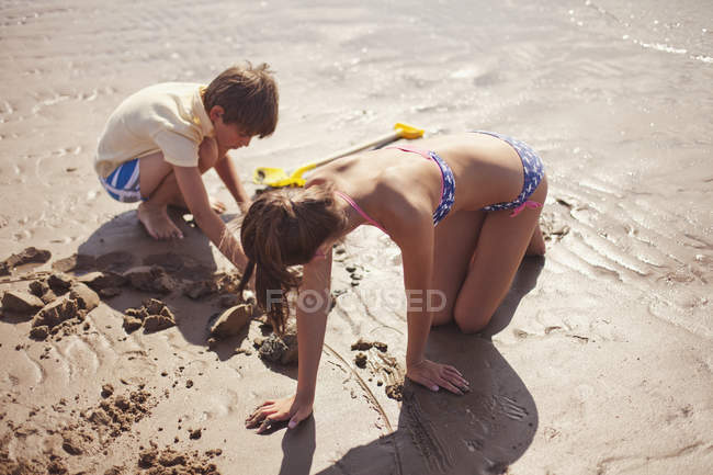 Irmão e irmã em roupa de banho brincando na areia molhada na praia ensolarada de verão — Fotografia de Stock