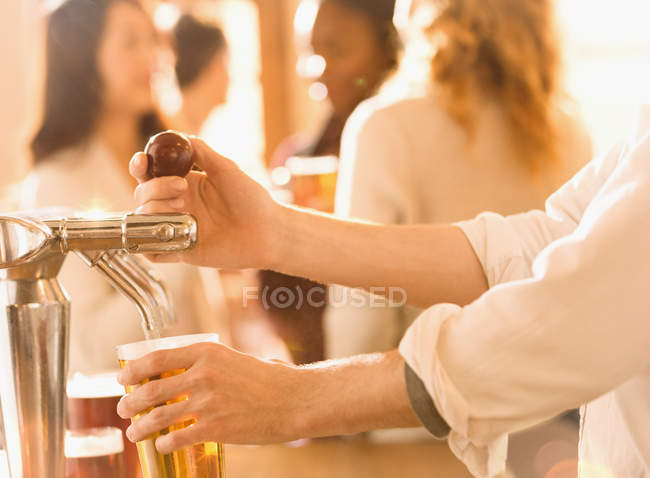 Imagem cortada de bartender derramando cerveja na torneira de cerveja no bar — Fotografia de Stock
