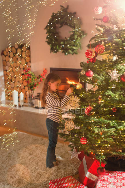 Girl hanging snowflake ornament on Christmas tree in living room — Stock Photo