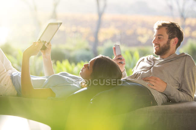 Colocação de casal e usando tablet digital e telefone celular no pátio ensolarado — Fotografia de Stock