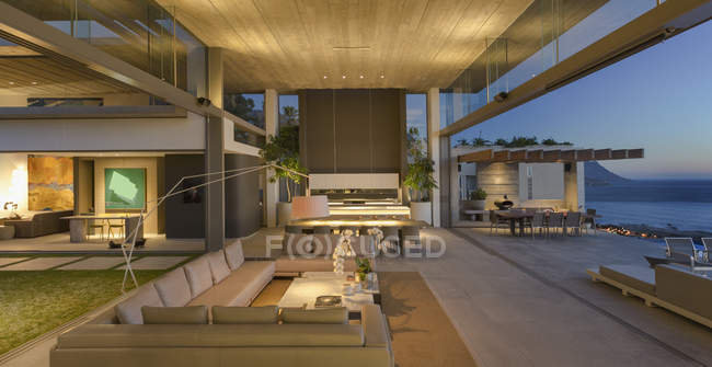 Illuminated modern, luxury home showcase interior living room open to patio at dusk — Stock Photo