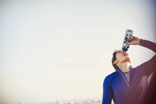 Thirsty male runner drinking water from water bottle below clear blue sky — Stock Photo
