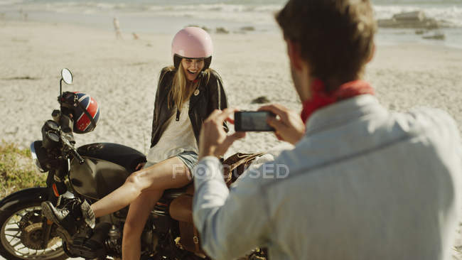 Молодой человек фотографирует женщину на мотоцикле на пляже — стоковое фото