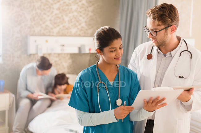 Arzt und Krankenschwester drehen im Krankenhaus ihre Runden und sichten Krankenakte auf Klemmbrett — Stockfoto