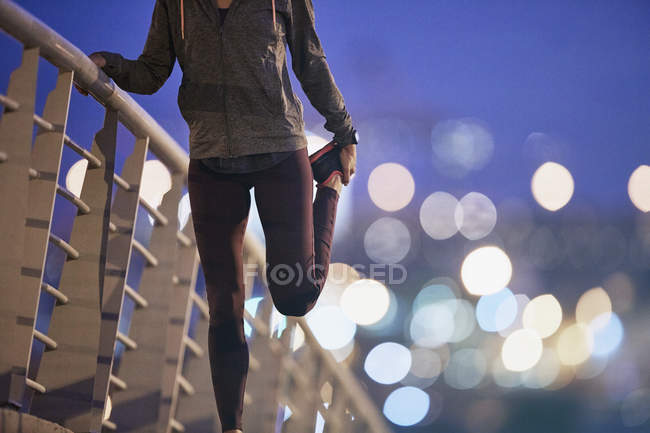 Жінка бігунка розтягує ногу на пішохідному мосту в сутінках — стокове фото