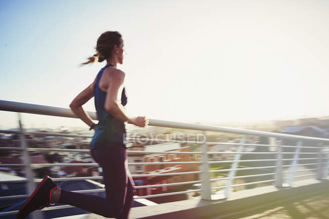 Бегущая женщина по солнечному городскому пешеходному мосту — стоковое фото