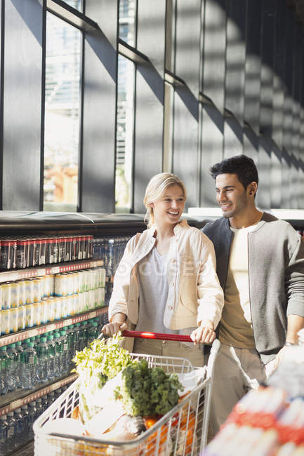 Young couple pushing shopping cart in grocery store market — Stock Photo
