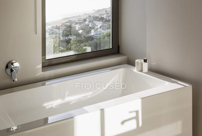 Reflejo soleado sobre bañera blanca moderna debajo de la ventana - foto de stock