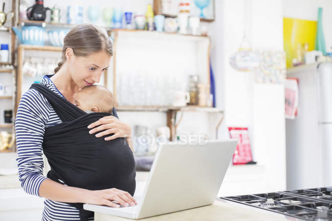 Mutter mit Baby benutzt Laptop in Küche — Stockfoto