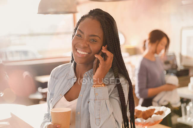 Усміхнена жінка розмовляє по мобільному телефону і п'є каву в кафе — стокове фото