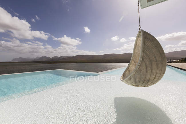 Сонячний, спокійний розкішний дворик з нескінченним басейном і підвісним сидінням з видом на океан — стокове фото