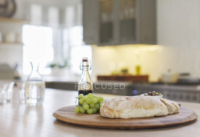 Baguette, balsamic vinegar and grapes on wooden board in kitchen — Stock Photo