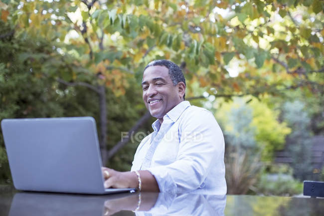 Homem sênior usando laptop na mesa do pátio — Fotografia de Stock