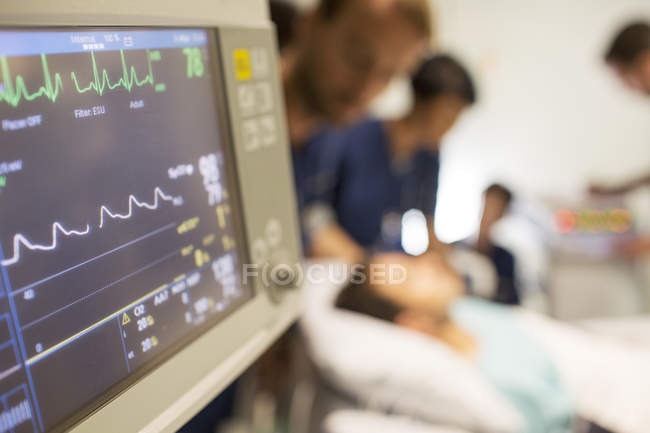 Heart rate monitor, patient and doctors in background in intensive care unit — Stock Photo