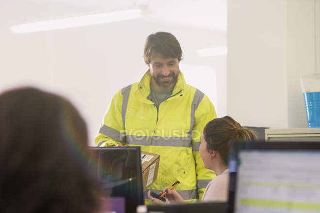 Deliveryman delivering package to businesswoman in office — Stock Photo