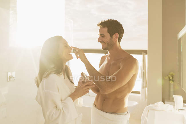 Пара игриво наносит увлажняющий крем в ванной комнате — стоковое фото