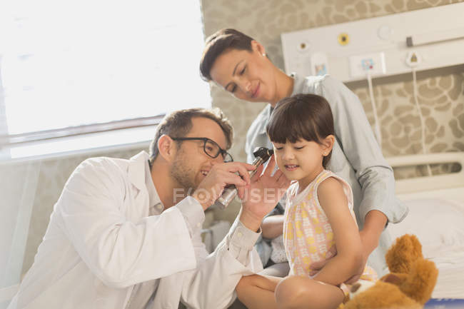Male doctor using otoscope in ear of girl patient in hospital room — Stock Photo