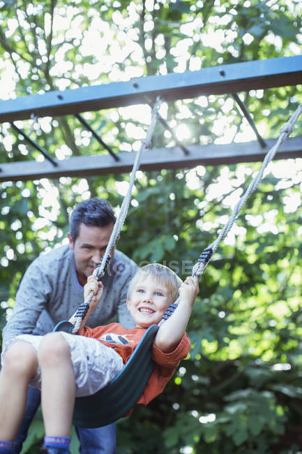 Padre spingendo figlio su swing all'aperto — Foto stock