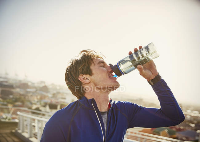Male runner drinking water on urban footbridge — Stock Photo