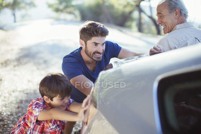 Des hommes de plusieurs générations poussent la voiture au bord de la route — Photo de stock