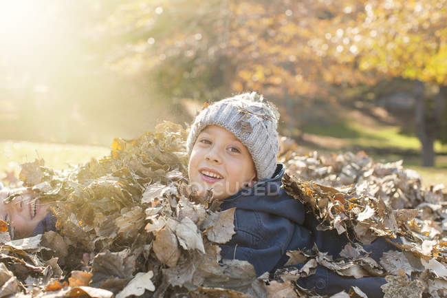 Portrait smiling boys covered in autumn leaves — Stock Photo