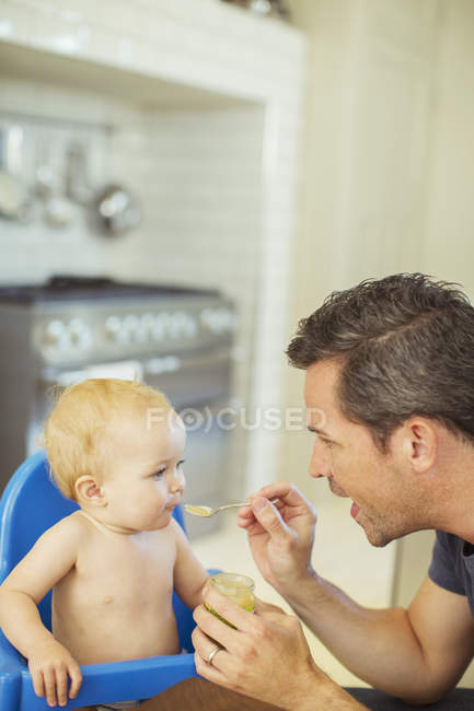 Pai alimentando bebê em cadeira alta — Fotografia de Stock