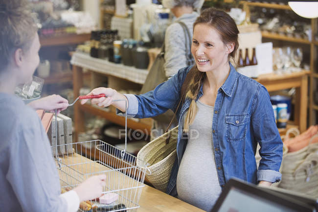 Mulher grávida dando cesta para caixa no balcão de check-out na loja — Fotografia de Stock