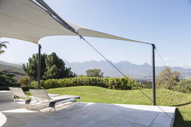 Sedie sdraio sotto tenda sul patio soleggiato con vista sulle montagne — Foto stock