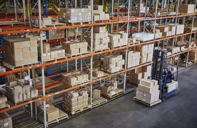 Рабочий вилочный погрузчик перевозит картонные коробки по полкам распределительного склада — стоковое фото