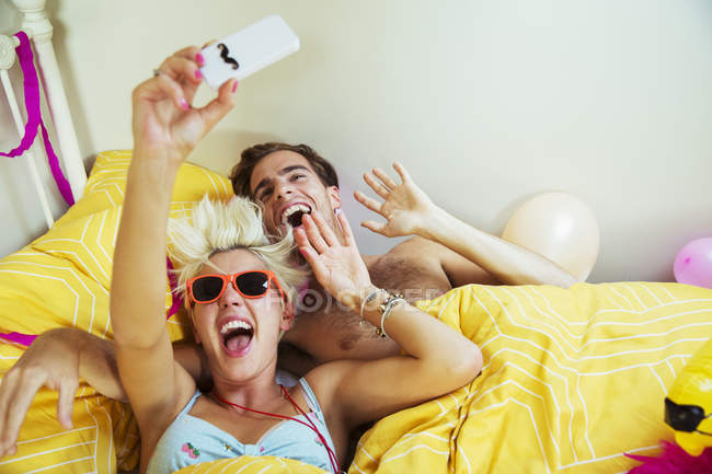 Couple taking self-portraits with smartphone in bed after party — Stock Photo
