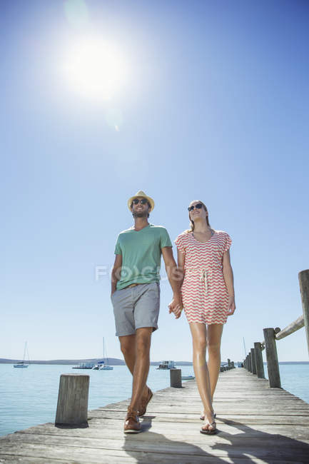 Couple holding hands walking along wooden dock — Stock Photo