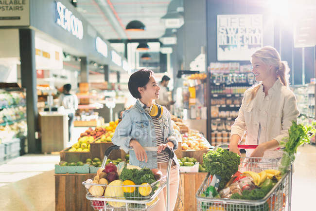 Young women friends with shopping carts talking in grocery store market — Stock Photo