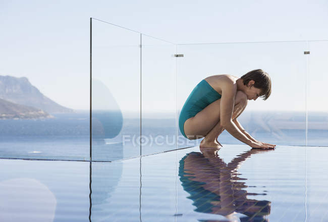 Woman crouching over infinity pool with ocean view — Stock Photo