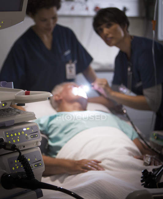 Médico examinando paciente sênior com lanterna na unidade de terapia intensiva — Fotografia de Stock