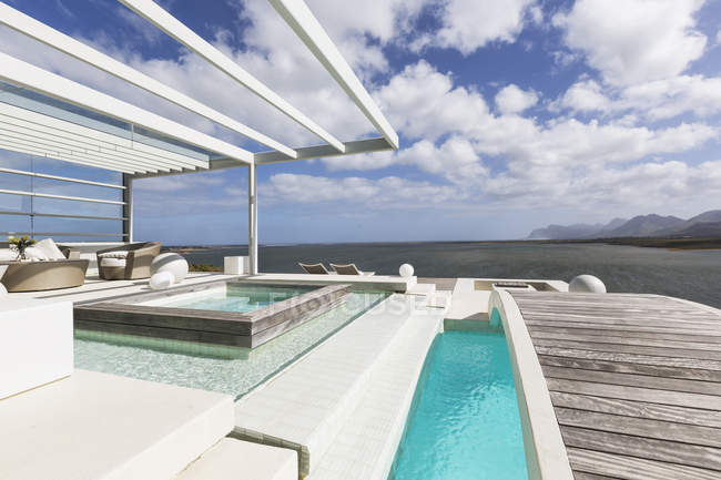 Солнечный, спокойный современный роскошный внутренний дворик с бассейном и пешеходным мостом с видом на океан — стоковое фото