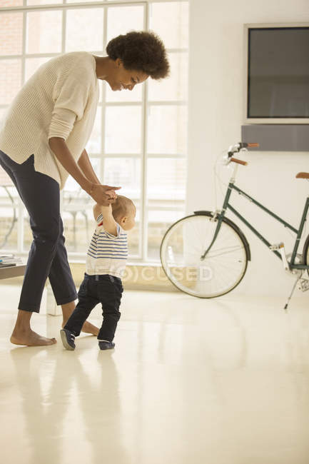 Mãe ajudando bebê menino andar na sala de estar em casa — Fotografia de Stock
