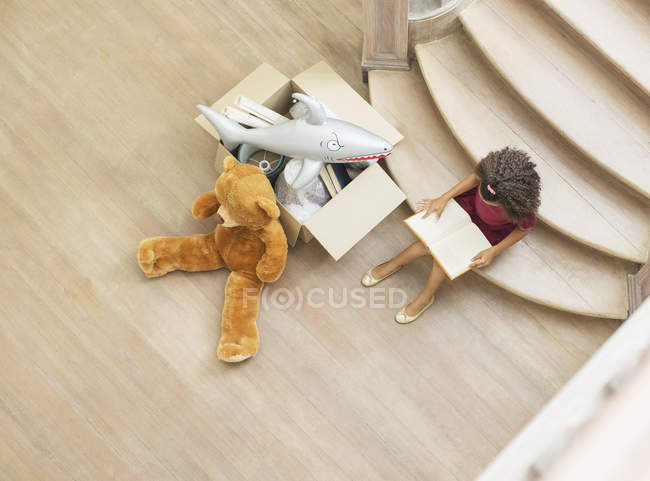 Молода дівчина читає на сходах з іграшками — стокове фото