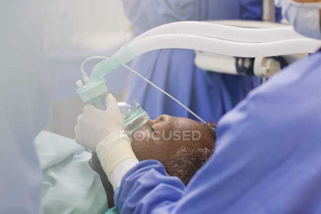 Крупним планом лікар носить хірургічні рукавички, тримаючи кисневу маску над пацієнтом в операційному театрі — стокове фото