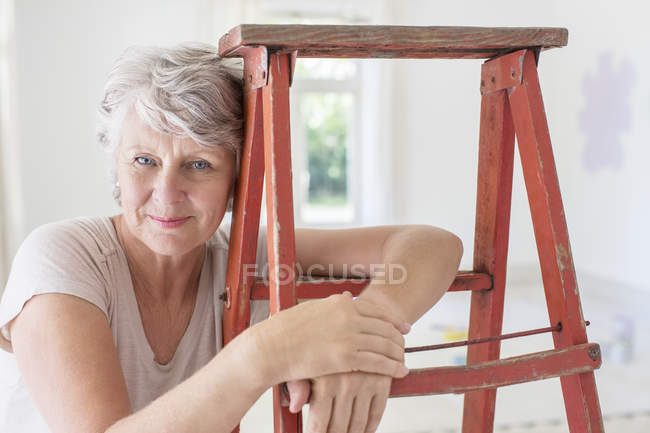 Ältere Frau lehnt auf Leiter im Wohnraum — Stockfoto