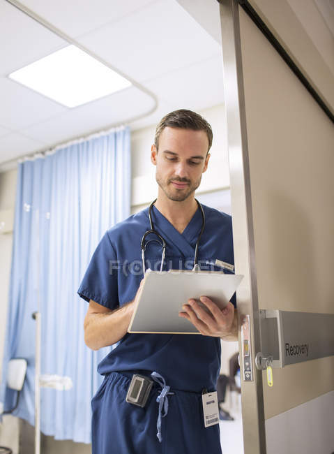 Médico de pé na porta, tomando notas no clip board no hospital — Fotografia de Stock