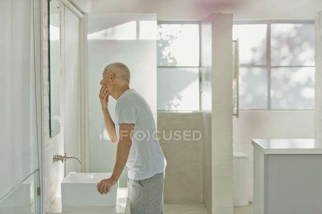 Зрілий чоловік торкається обличчя у дзеркалі ванної кімнати — стокове фото