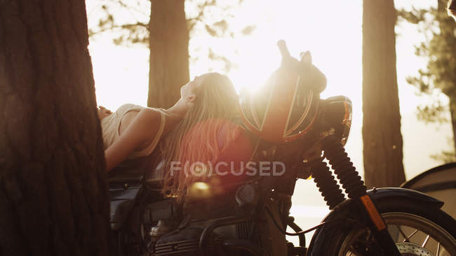 Young woman laying on motorcycle under sunny trees — Stock Photo