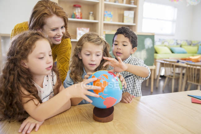 Students and teacher examining globe in classroom — Stock Photo