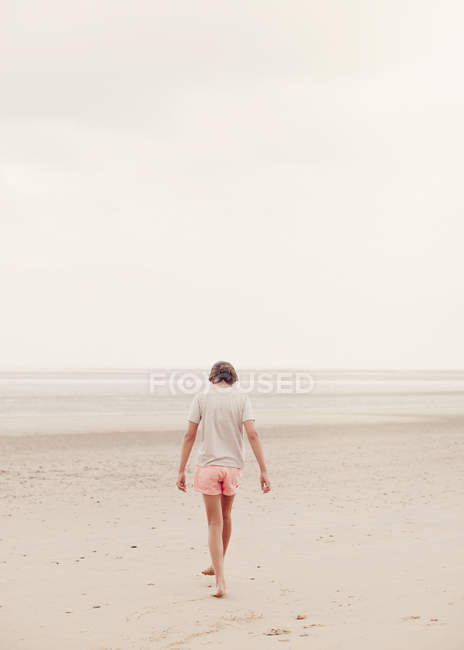 Ragazza adolescente che cammina nella sabbia sulla spiaggia estiva nuvolosa — Foto stock