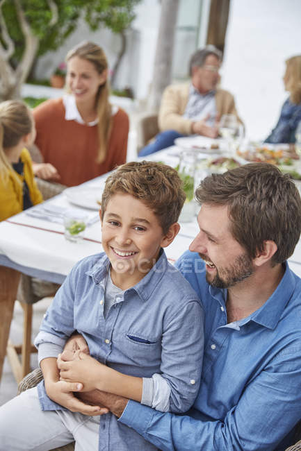 Портрет улыбающихся отца и сына, наслаждающихся обедом в патио — стоковое фото