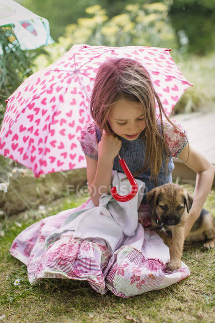 Girl with puppy dog holding heart-shape umbrella in grass — Stock Photo