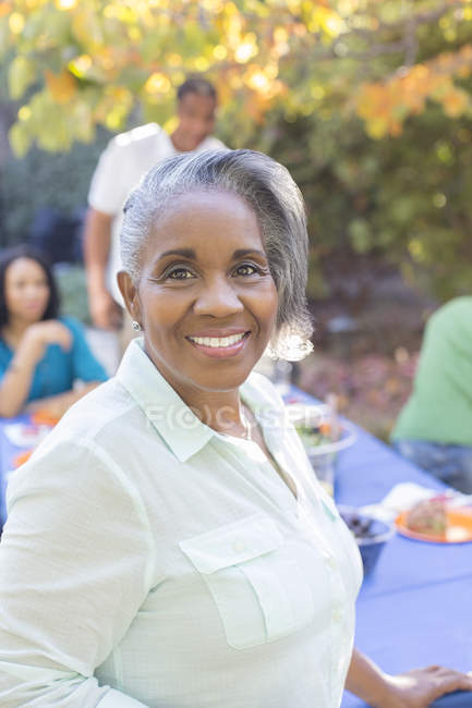 Close up portrait of smiling senior woman on patio with family in background — Stock Photo